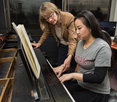 A student gets assistance on the piano from a faculty member.
